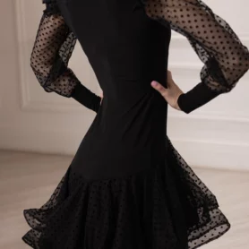 Деталь черного платья для бальных танцев с прозрачными сетчатыми рукавами в горошек и расклешенной юбкой.