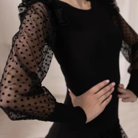 Крупный план черного платья для бальных танцев с прозрачными сетчатыми рукавами в горошек и декоративными воланами.